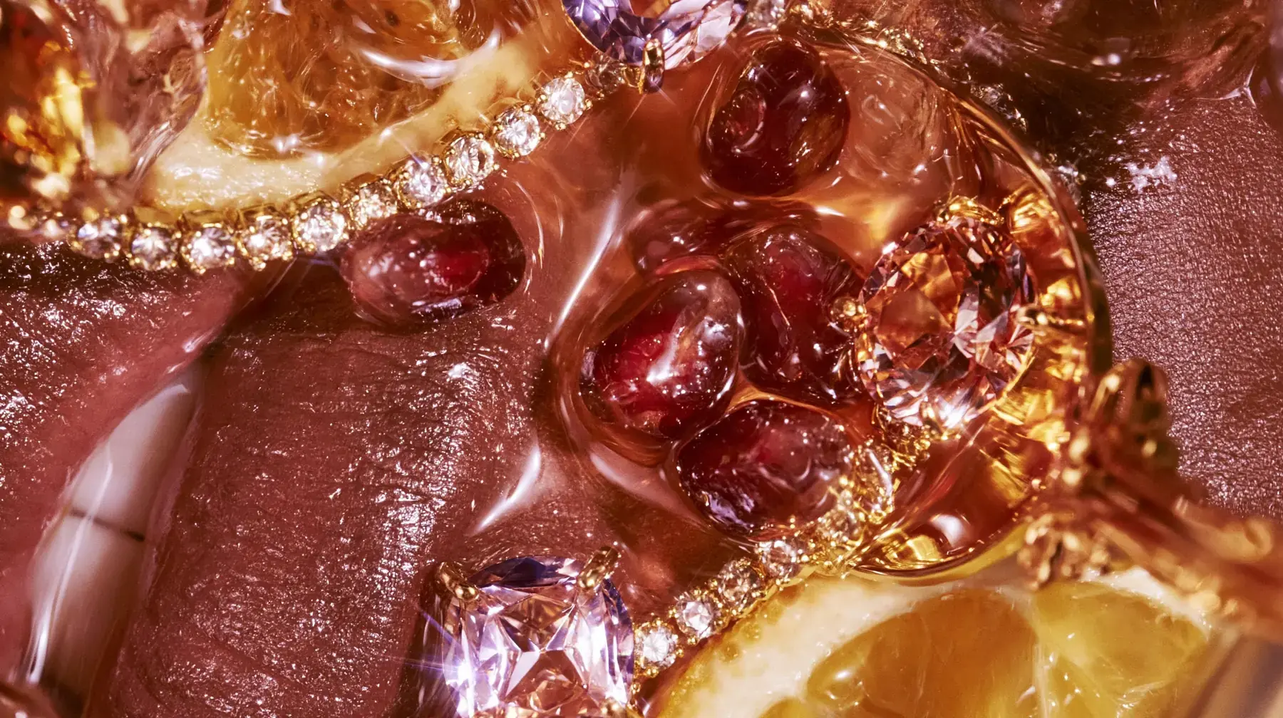 Glossy lips, gold chains, faceted gems and pomegranate seeds in amber liquid